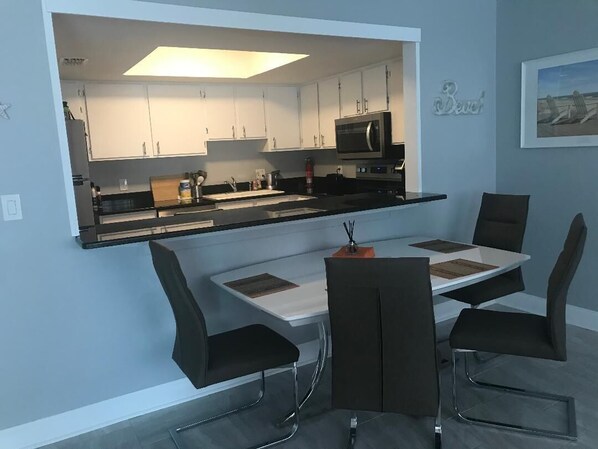 Una cocina moderna con armarios blancos, encimera negra y un comedor con mesa y sillas.