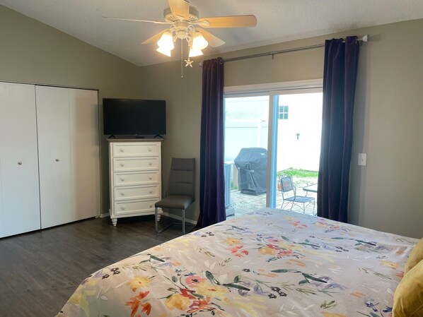 Une chambre à coucher avec un lit, une commode, une chaise, un ventilateur de plafond et un téléviseur fixé au mur.