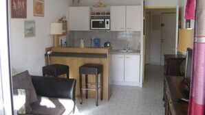 A compact living space with a kitchenette, a dining area with two stools, a sofa, and a television. - 2 ROOMS+CABIN-AIR CONDITIONING- SWIMMING POOL- SOUTH-FACING TERRACE- LOVELY LAKE VIEW, WIFI. (La Grande-Motte)