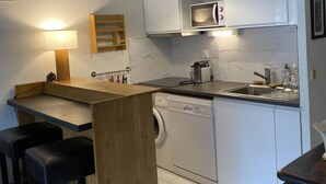 A compact kitchen with a built-in dishwasher, a microwave, and a sink. There is a wooden bar counter with stools, and a hanging pendant light above the counter. - 2 ROOMS+CABIN-AIR CONDITIONING- SWIMMING POOL- SOUTH-FACING TERRACE- LOVELY LAKE VIEW, WIFI. (La Grande-Motte)