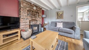 Una sala de estar con chimenea de ladrillo, televisor de pantalla plana, sofá gris y una mesa de centro de madera.