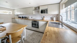 Una cocina moderna con armarios blancos, encimera de madera, microondas integrado y pileta de acero inoxidable.