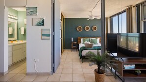 A hotel room with a bed, a television, a plant, and a bathroom visible through an open door.