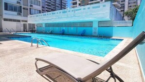 A swimming pool with lounge chairs and a covered area, surrounded by high-rise buildings.