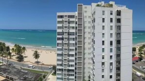 A high-rise building with a beach view, featuring multiple balconies and a clear blue sky.