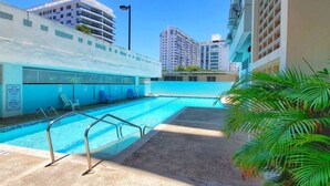A swimming pool with a clear blue water, surrounded by a concrete deck and palm trees. - Luna Llena Beach 1BDR Oceanview Pool (Isla Verde)