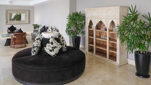 Un salon moderne avec un canapé noir rond, une chaise en bois, un grand miroir et deux plantes en pot.