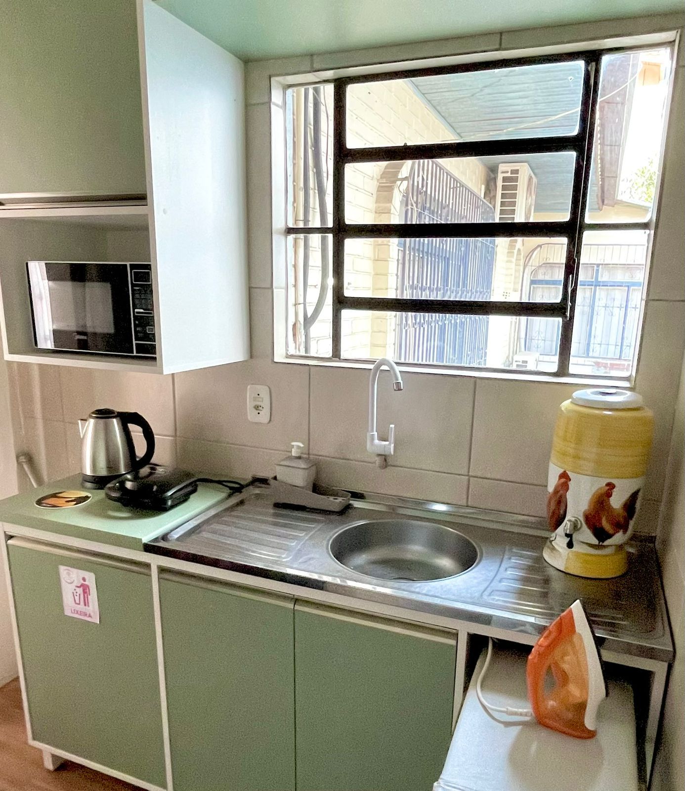 Cocina compacta con microondas integrado, pileta y ventana con vista a edificios.