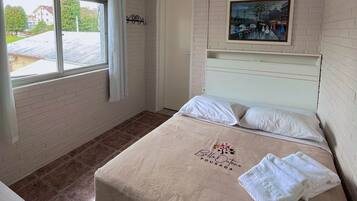 A bedroom with a bed, a window, an air conditioner, a painting, and a towel on the bed.