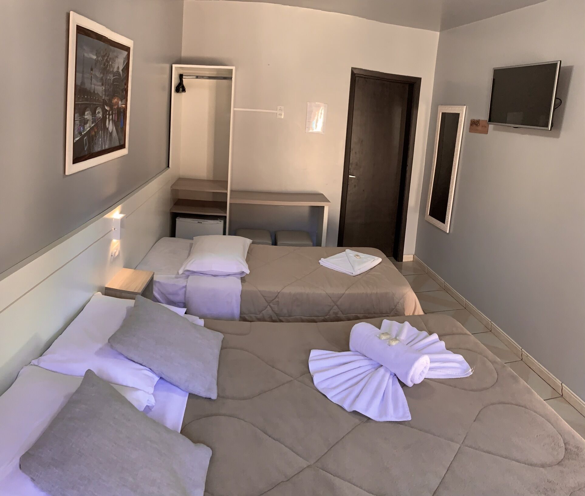 A hotel room with two beds, a mirror, a TV, and a door.