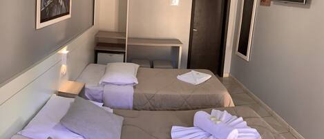 A hotel room with two beds, a mirror, a TV, and a door.