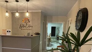 A reception area with a counter, a potted plant, and a wall with a logo. - Pousada Bello  Outono (Canela)