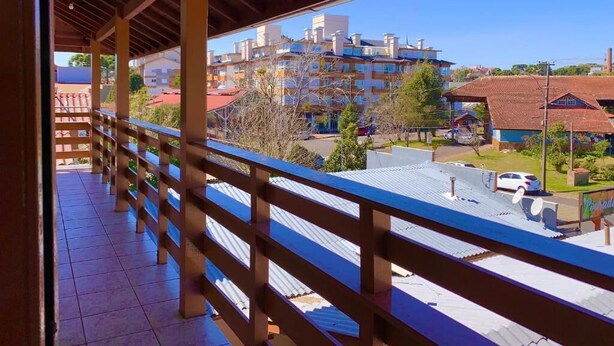 A covered balcony with a view of a residential area, including a multi-story building and a parking lot. - Pousada Bello  Outono (Canela)