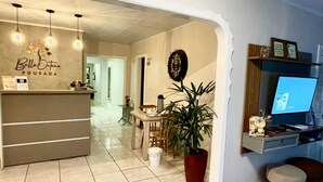 A reception area with a desk, a potted plant, a dining area with a table and chairs, and a television on a stand. - Pousada Bello  Outono (Canela)