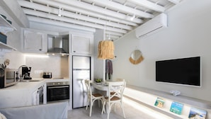 Eine moderne Küche mit weißen Schränken, einem Essbereich mit weißen Stühlen, einem Flachbildfernseher und einer Decke mit freiliegenden Balken.
