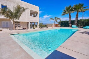 A modern pool area with a clear blue pool, a two-story building with balconies, and palm trees. - VILLA CIURIDDA (Alcamo)