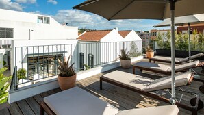 Terraza en la azotea con sillones de relax y plantas en macetas, con vistas a un paisaje urbano.