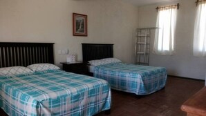 A room with two beds, a wooden headboard, a framed picture on the wall, and a window with curtains.