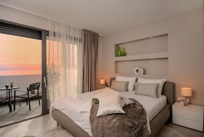 Quarto de hotel moderno com uma cama grande, varanda e uma vista, e uma pequena mesa com cadeiras.