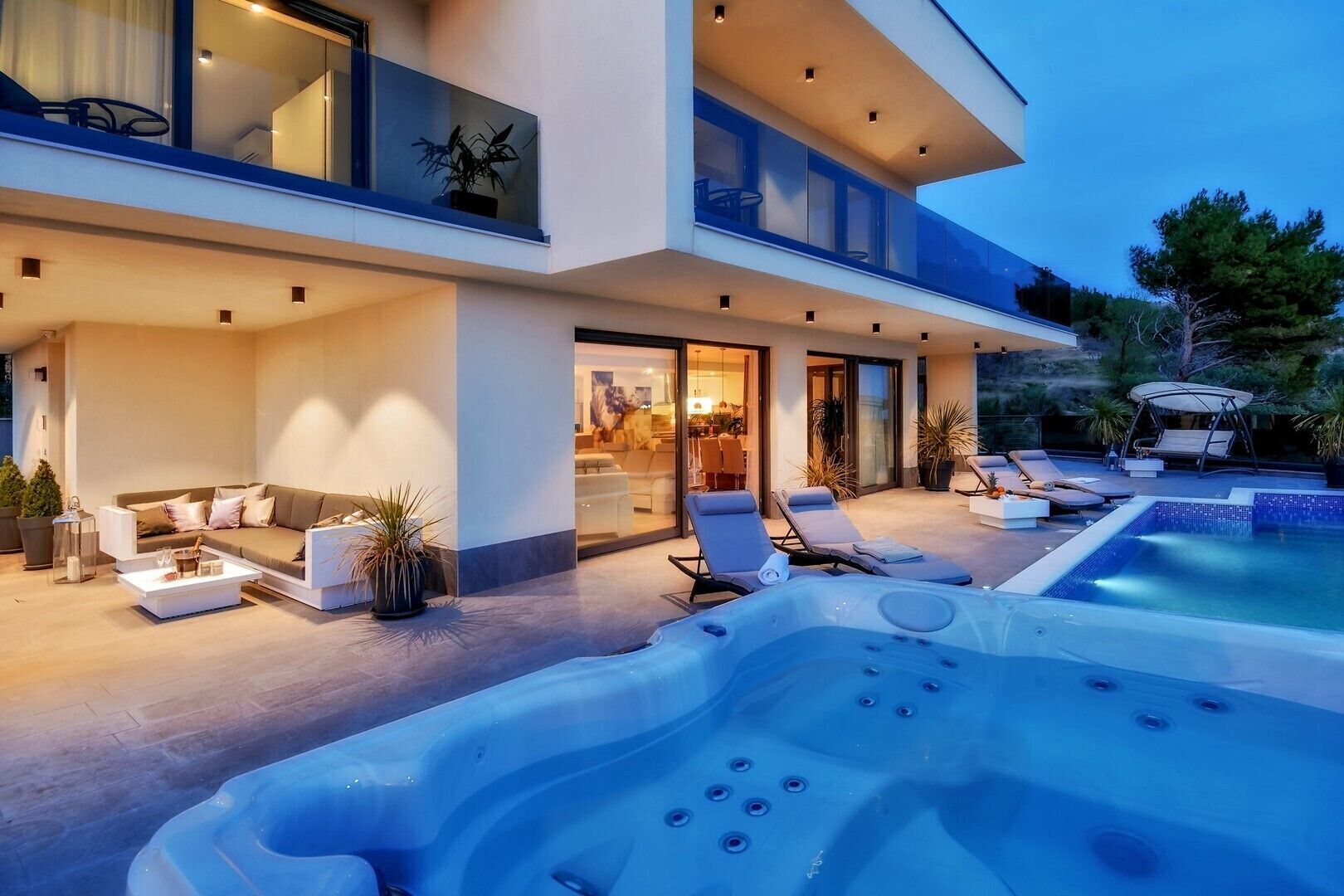 A modern two-story house with a swimming pool, outdoor seating, and a hot tub.