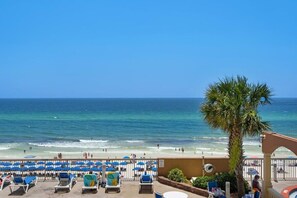 A beach view with lounge chairs and umbrellas, a palm tree, and a clear blue sky. - Coastal Condo 807 | Beachfront! (Panama City)