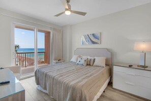 Un dormitorio con cama, mesita de noche, lámpara, ventilador de techo y vista al océano a través de una puerta corrediza.