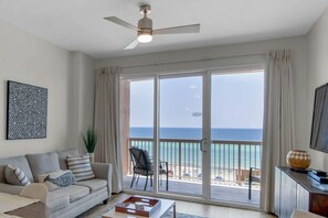 A living room with a sofa, a coffee table, a ceiling fan, and a large sliding glass door leading to a balcony with a view of the sea.