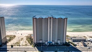 A high-rise hotel with a beach view, multiple balconies, and a parking lot.