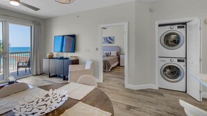 A modern hotel room with a dining area, a TV, a washing machine, and a view of the sea.