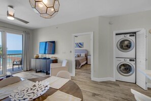 A modern hotel room with a dining area, a TV, a washing machine, and a view of the sea.