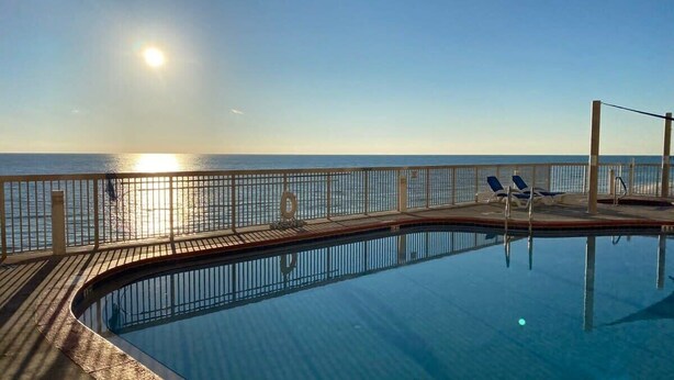 A swimming pool with a wooden deck and lounge chairs, overlooking a body of water.