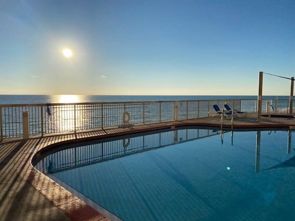 A swimming pool with a wooden deck and lounge chairs, overlooking a body of water.