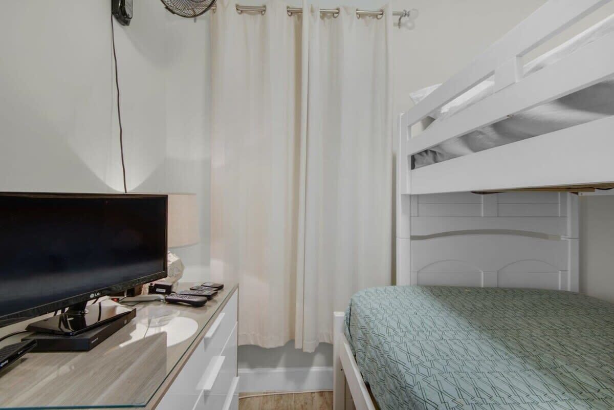 A room with a bunk bed, a desk with a flat-screen TV, and a curtain.