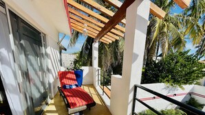 A balcony with a red-striped lounge chair, a potted plant, and a view of palm trees and a building. - 2 bed, 2 bath house w/ private pool, pyramid waterfall, short walk to beach. (Barra de Navidad)