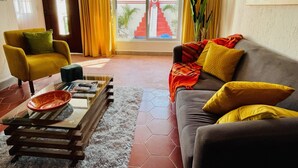 A living room with a yellow armchair, a grey sofa with yellow cushions, a glass coffee table with magazines and a bowl, and a view of a red staircase outside. - 2 bed, 2 bath house w/ private pool, pyramid waterfall, short walk to beach. (Barra de Navidad)