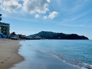 Una playa con orilla arenosa, mar tranquilo y una montaña al fondo.