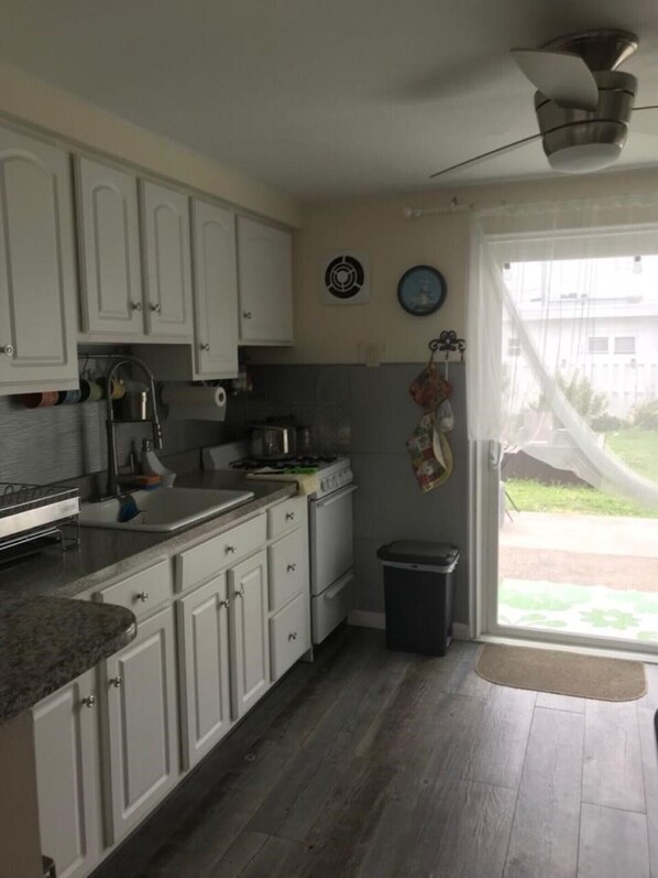 A kitchen with white cabinets, a stove, a sink, and a trash bin. There is a window with a view of the outside. - 1 block from the beach . Ocean view cozy beach house . Backyard with fire pit . (Wildwood Crest)