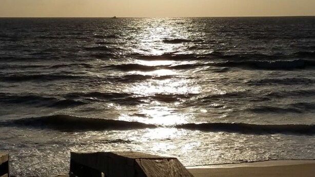 A wooden pier extending into calm waters with the sun low on the horizon.