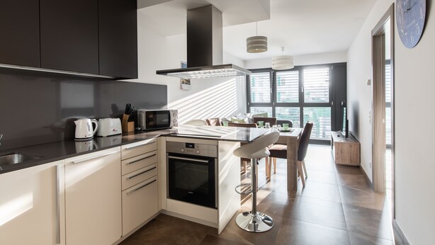 Una cocina moderna con una isla central, un comedor con una mesa alta y sillas, y un ventanal que proporciona luz natural.