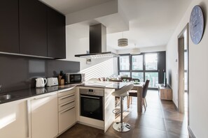 A modern kitchen with a central island, a dining area with a high table and chairs, and a large window providing natural light.