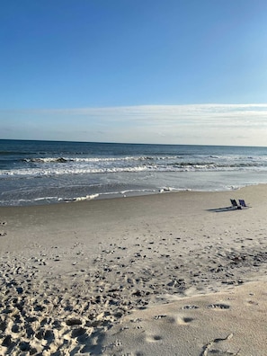 Ein Strand mit Fußabdrücken und zwei Liegestühlen.