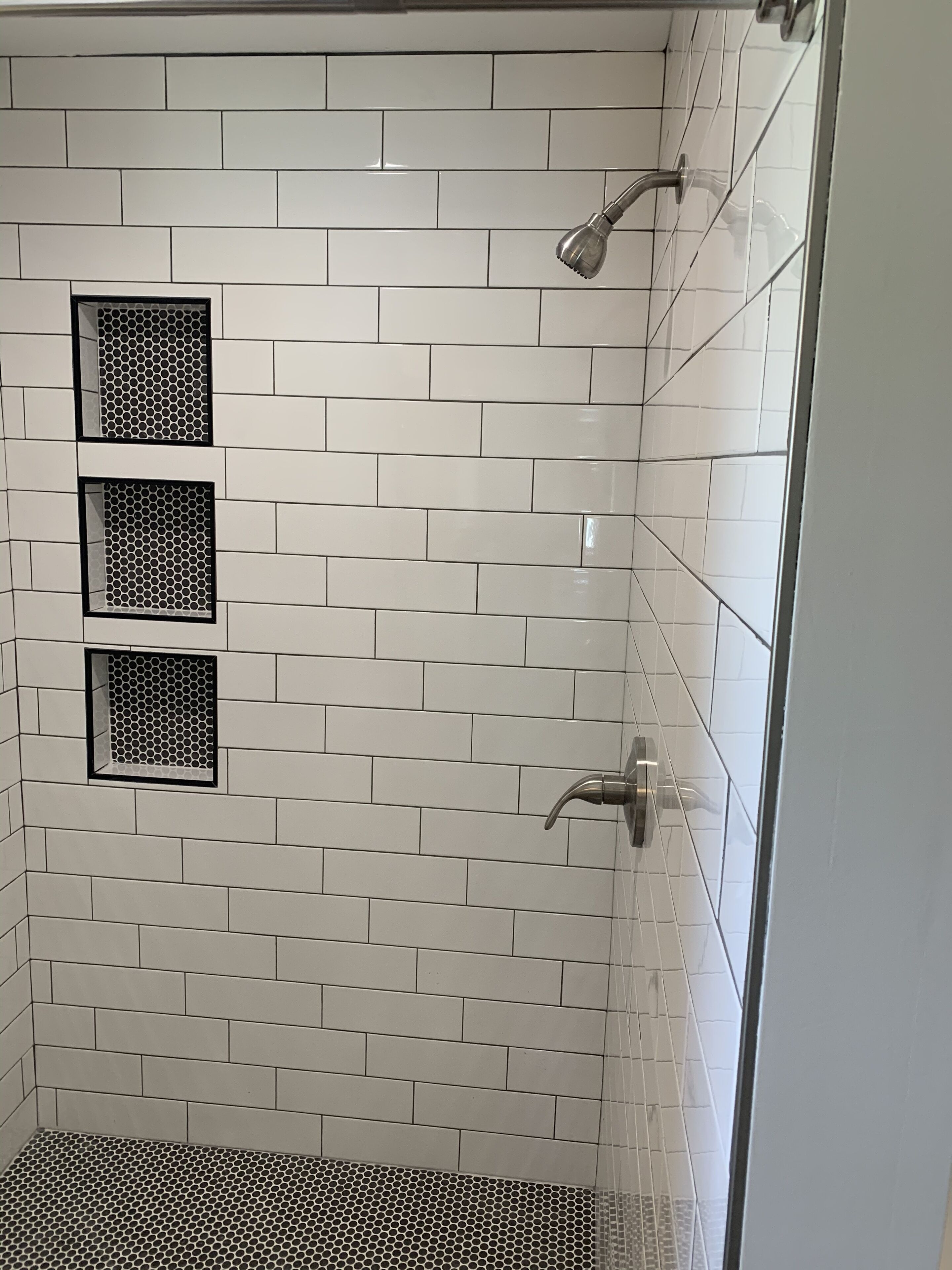 Ducha con azulejos blancos tipo metro y piso con estampado blanco y negro.