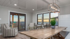 A spacious dining area with a large wooden table, striped armchairs, and a view of the water through large windows.
