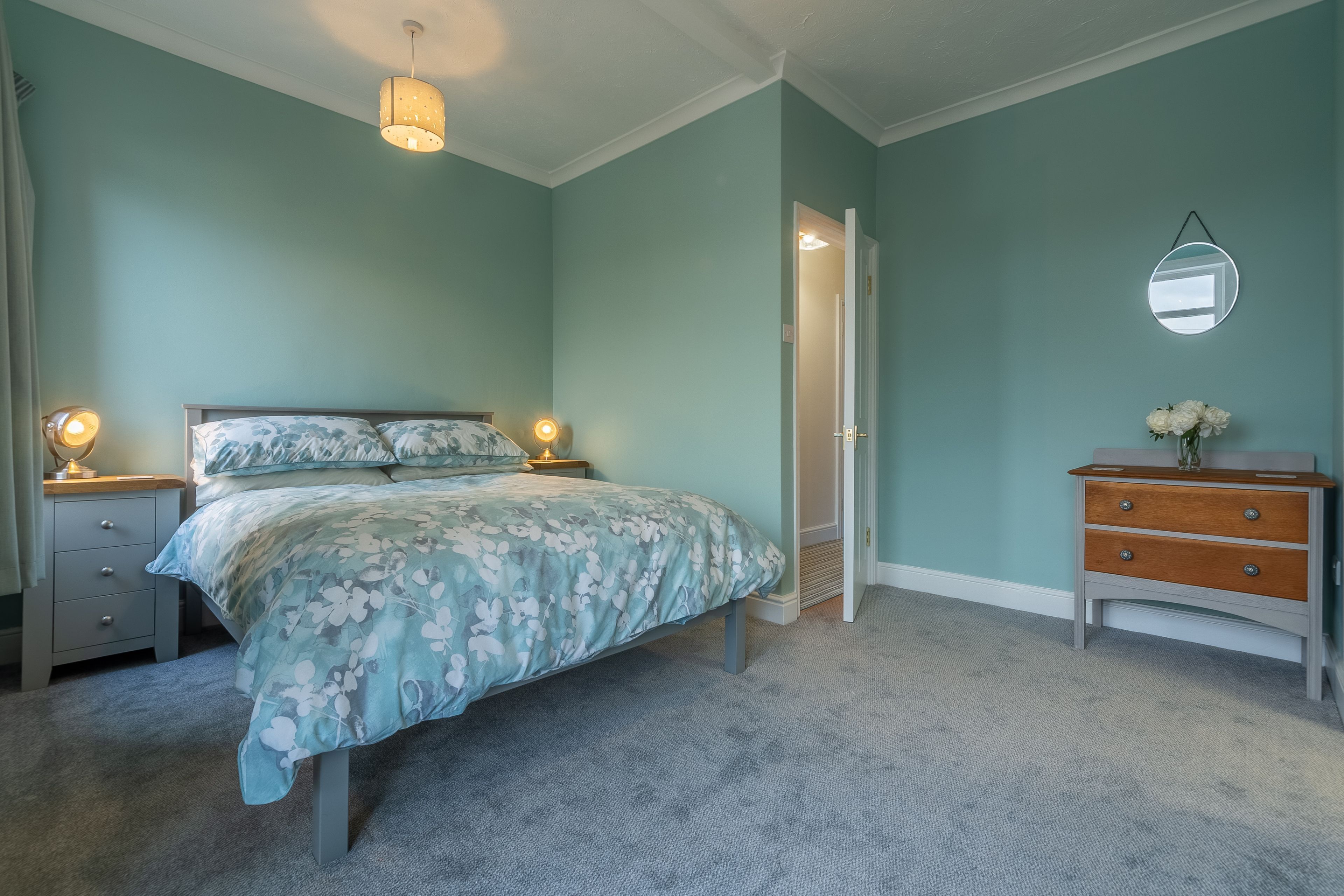 Een slaapkamer met een bed, bedlampjes, een kaptafel en een spiegel aan de muur.