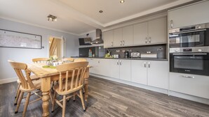A modern kitchen with white cabinets, a Bosch oven, and a dining area with wooden chairs and a table. - Heacham Hidey Hole, Heacham, Norfolk (Heacham)