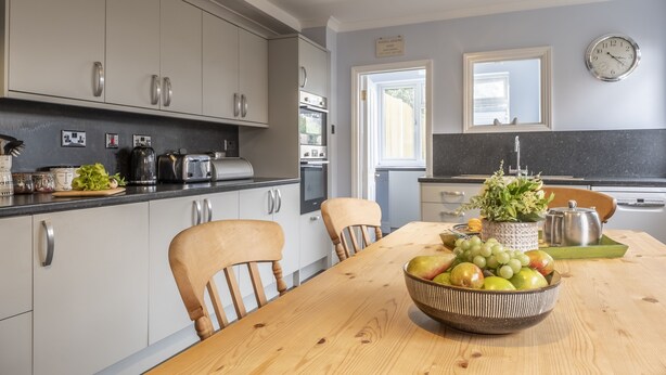 A modern kitchen with white cabinets, a wooden dining table, and a bowl of fruit. - Heacham Hidey Hole, Heacham, Norfolk (Heacham)