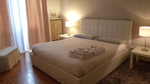Een hotelkamer met een groot bed, twee bedlampen, een radiator en een kleine tafel met een lamp.