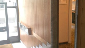 Een gang met houten lambrisering, een trap en een deur die leidt naar een kamer met een betegelde vloer.