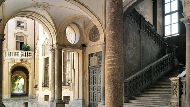 Een interieur met klassieke architectuur, inclusief kolommen, bogen en een statige trap.
