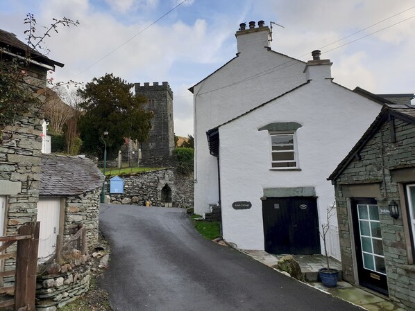 A narrow street with stone buildings, including a white house with a black door and a sign reading "Ann's Cottage."
